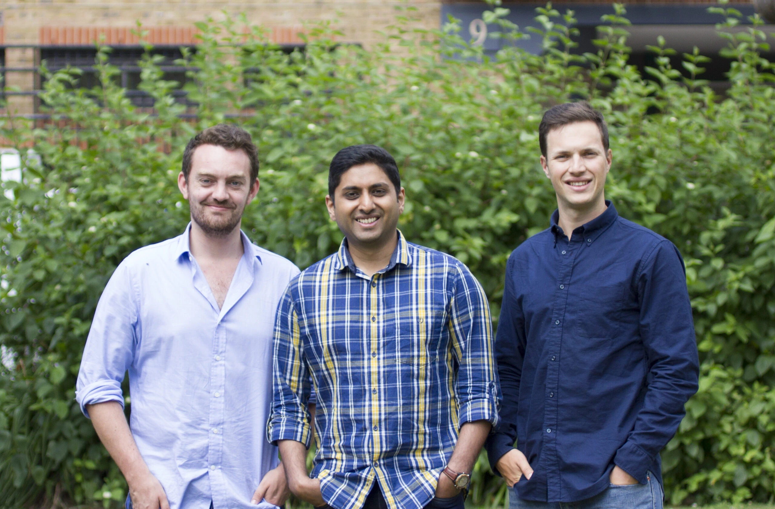 Three men standing outdoors in front of greenery, with the Pouch founders among them