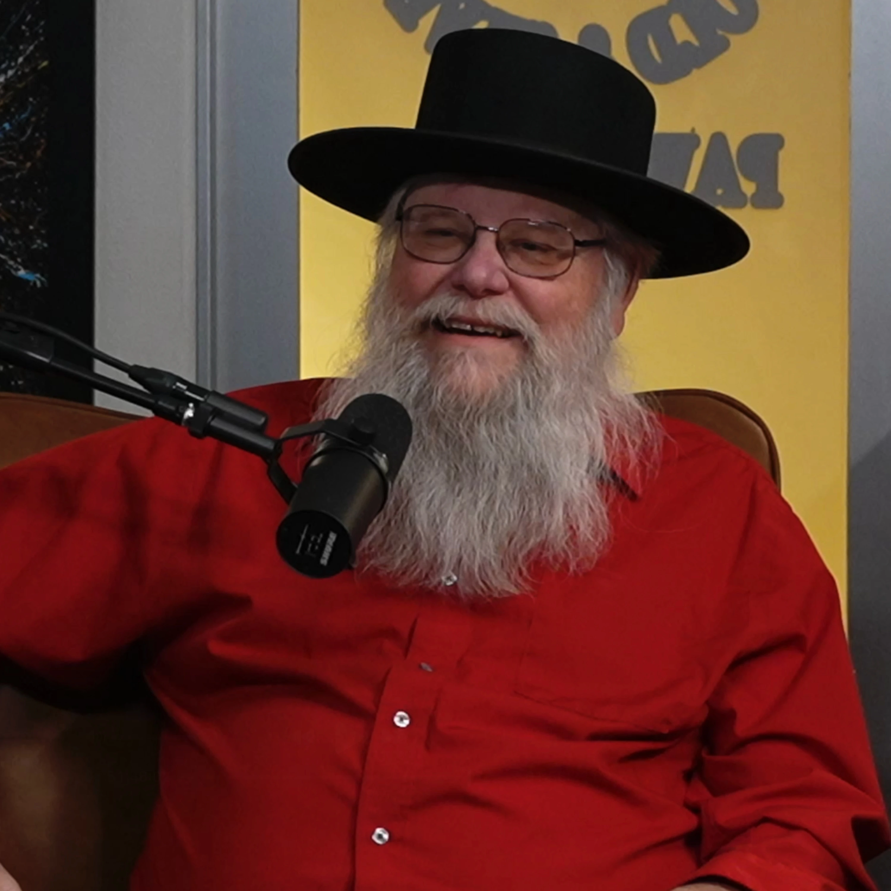 Mark Hall-Patton wearing a black hat and red shirt, seated at a microphone during a podcast interview